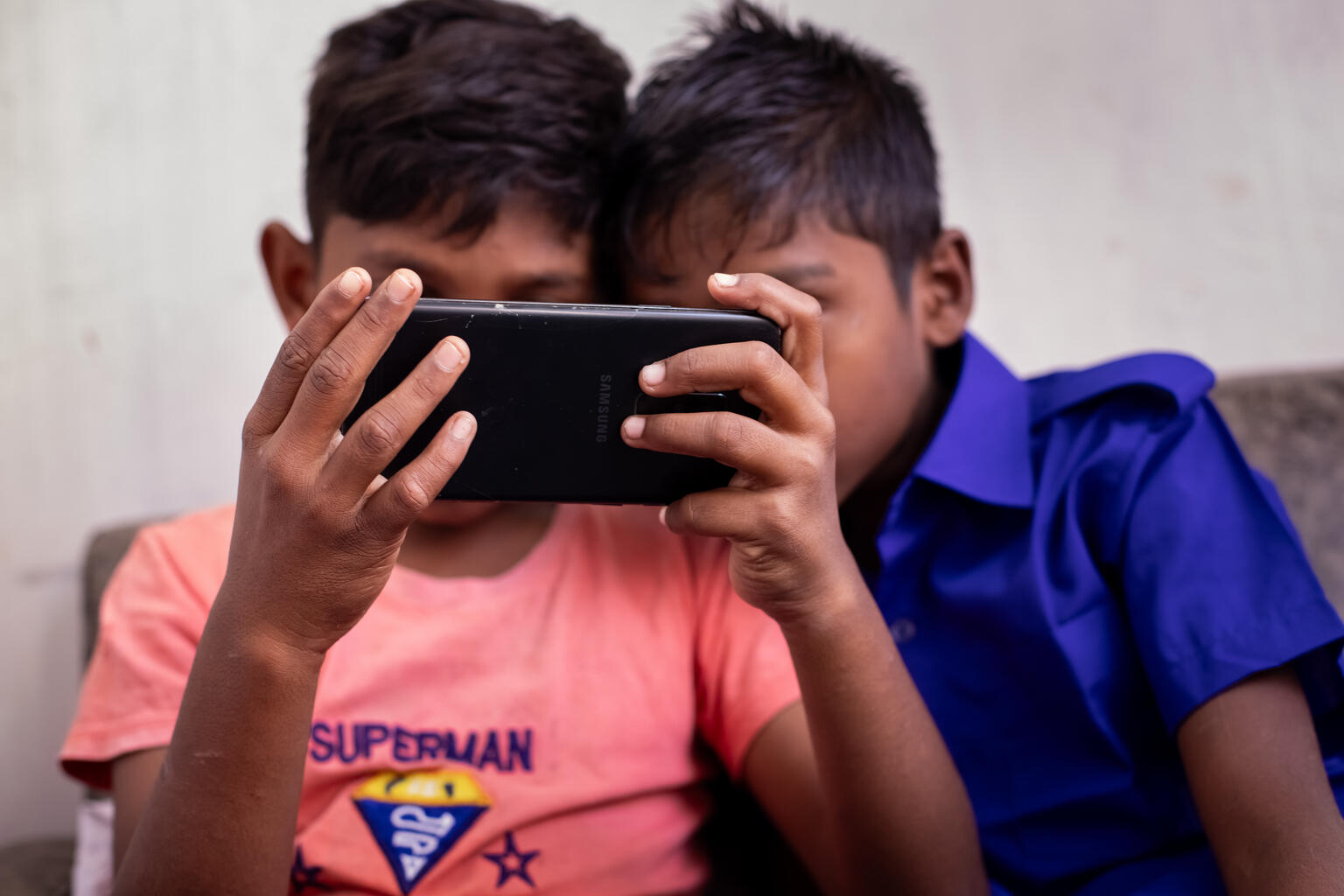 スマートフォンで再生されている動画に見入る男の子たち（バングラデシュ、2025年11月25日撮影）