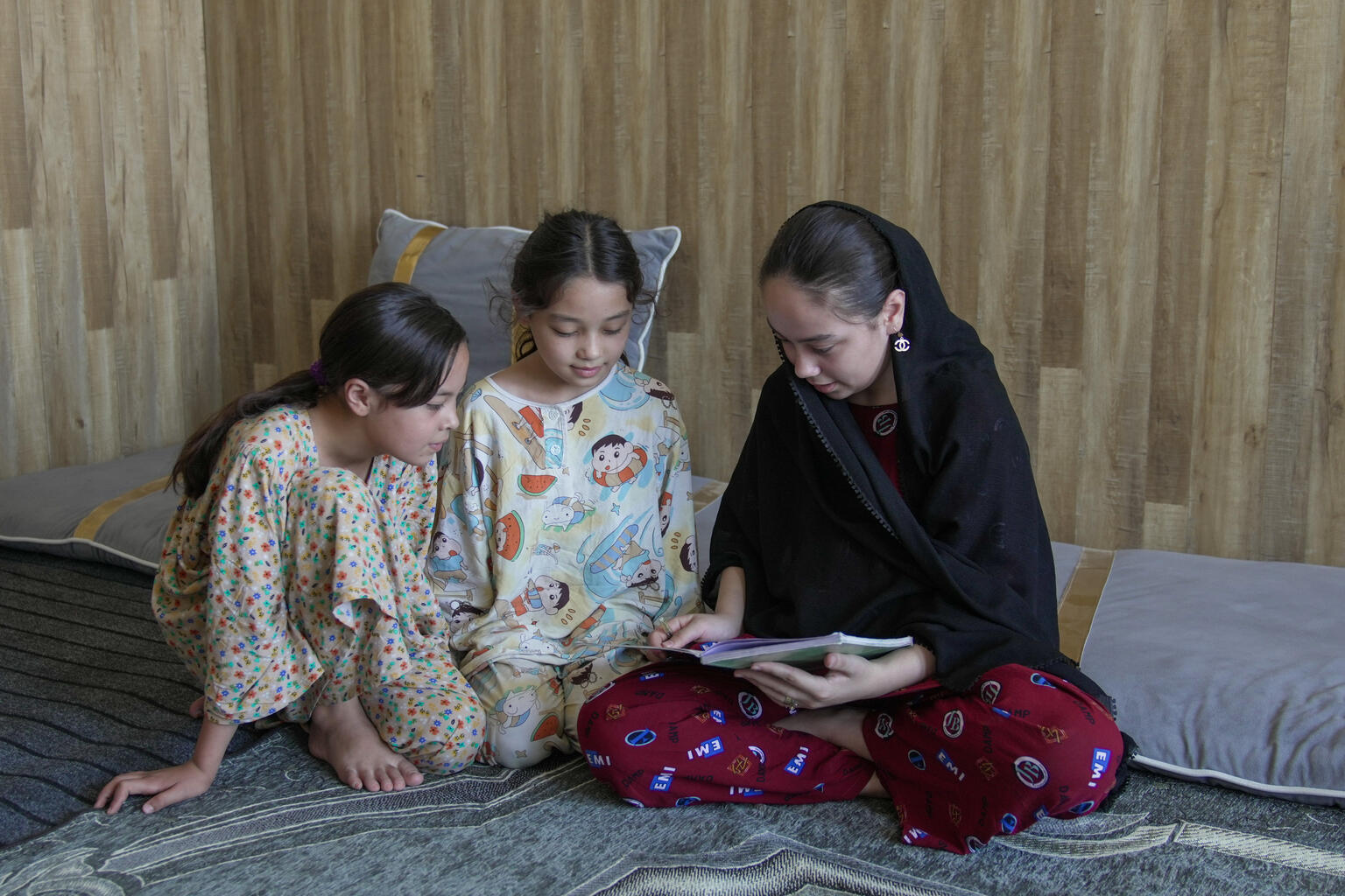 妹たちの勉強を見ている14歳のカウサルさん。女子中等教育が禁止されているため、小学6年生の課程修了後は自宅で過ごしているが、将来は助産師となって、地域の女性たちを支えたいと願っている(アフガニスタン、2026年7月23日撮影)