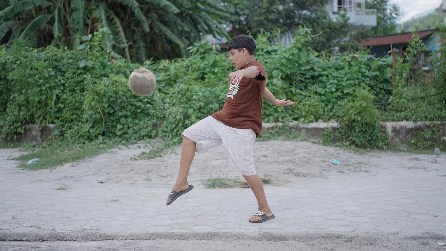 サッカーボールを蹴る14歳のスウォスティク・パウデルさん。土石流に巻き込まれたが、一命をとりとめた(ネパール、2026年8月30日撮影)