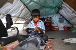 仮設テントの中で本を読む男の子。