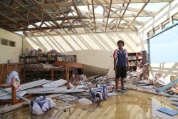 サイクロンの被害に遭い、瓦礫や本が散乱する学校の図書館にたたずむ高校生の少女。