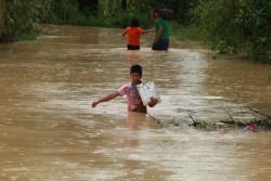 荷物を抱えて台風で洪水が起こった村の中を歩く少年。（フィリピン）