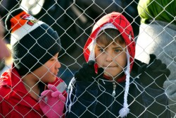 難民のための施設の近くにあるフェンスから外を眺める男の子たち。
