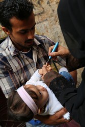 ポリオの予防接種を受けた“しるし”を赤ちゃんの小指に付ける保健員。（シリア）