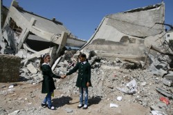 破壊された学校の前で、手をつなぐ10歳の女の子。（ガザ地区）