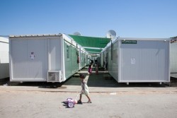 アテネのスカラマンガス難民キャンプ内の仮設住居の前で人形を連れて歩く女の子。