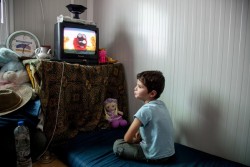 仮設のコンテナ式住居でテレビを見るカルムくん（5歳）。