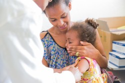 エチオピアで母親に抱かれながら麻疹の予防接種を受ける女の子。