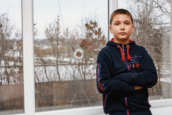 学校に残る銃痕の脇に立つ男の子（ウクライナ・ドネツク州）