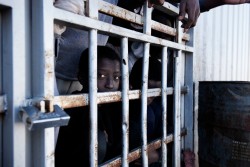A migrant looks out from behind the bars of a cell at a detention centre in Libya, Tuesday 31 January 2017. The detention centre was constructed in 2006 following an agreement between the Italian and Libyan governments in an attempt to stem the flow of migrants reaching Italy. When UNICEF visited the centre on 31 January 2017, the population consisted of 27 women (four of whom were pregnant), one 11-month old child, a four year old, as well as 1,352 men - of which 250 were under the age of 16. The centre is at the crossroads of areas controlled by different militias fighting with each other. For this reason it is a very dangerous centre, for officers who work there and for migrants in detention. The detention centre is currently managed by the Libyan National Army, and most migrants remain there for a period of 8 to 10 months according to the manager Abdalhamad Altunisa. "Children are often alone, they cross 2000 kilometres of desert without their families, and they are rescued at sea without documents, said Altunisia this makes it difficult for us to know their real nationality and age. Before 2014 we brought them back to the border between Nigeria and Libya to take them back to their countries, but after the last civil war it was much more difficult. Those areas are dangerous even for us. Migrants who were being held in the cells said they are rarely allowed out. Many of the those being held are sick, and some detainees are said to have passed away because they have no access to medical care. The director of the centre, Altunisa, said "the official government [of Sarraj] does not give us the money to pay salaries and to pay those who bring us food. So often we do not have enough food or drinking water. This winter was particularly cold and in recent weeks 15 migrants froze to death." Libya is a country in turmoil. Since 2014 security is precarious, living is hard, and violence is commonplace. The country is riven with militias in conflict with each oth