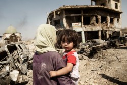 A woman carries her child through the debris of buildings and vehicles destroyed during intense fighting as they flee the Old City for safe areas in Mosul, Iraq, Thursday 6 July 2017. Partially visible at left is the destroyed Great Mosque of al-Nuri. The end of the violence in Mosul in July 2017 is likely to be a turning point for Iraq, but it will not bring the guns to silence as the battle will soon turn to Tal Afar, West Anbar and Hawija. Three years of traumatic experiences and months of intense fighting have left children and families in Mosul struggling with the physical and psychological wounds of war, with childhoods turned into nightmares of brutality, displacement and loss. Many are being treated in trauma centres in west Mosul with bullet and shrapnel wounds are children and many children who fled the intense fighting between government and non-government actors are severely distressed and need psychosocial care. Warring parties actively recruited children into the fighting, depriving them of a normal childhood and the chance of a better future.Some children are being held in detention centres. UNICEF is providing these children with legal representation, education, psychosocial assistance, vocational training, and helping to improve the conditions of the facilities where children are held. Providing schools, water, sanitation and health services will be crucial for all Iraqi children and their families to return home. Otherwise, the risk is not only of a lost generation, but also severely restricted opportunities to build a solid foundation for coexistence, tolerance and peace in the future.