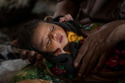 [DRAFT CAPTION] Kismat Ara, finally fed, becomes quiet again. The mother, glassy-eyed, in pain, perhaps traumatized turns away. The grandmother soothes both of them.  Story Header: This sequence of photographs follows the newborn Rohingyan infant Kismat Ara from the Unicef supported Birthing Centre to her new home in a refugee camp. Along the way she is separated from her suffering mother, carried in the arms of her grand-mother who loses her way in the labyrinth of the Kutupalang refugee camp, caught in the rain, with a newborn in her arms. With the help of a health volunteer she eventually was reunited with the exhausted, terrified mother at her tent. NOTA BENE there is an short essay on this by Samin Sababa to go with it, so specific captions are kept short as details are in the story.