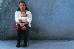 [RELEASE OBTAINED] On 9 October 2016, 6 month old Luis Zambrano  looks up to his mother, Esmeralda Zambrano. They are seated in front of a concrete wall in the living area of their home in Puebla, Mexico.  Esmeralda takes part in UNICEF-led program that utilizes innovation and mobile phones to track their Child's development needs and are involved in weekly meetings to discuss questions and needs. The baby is wearing tiny red sneakers and holding a brightly colored maraca. UNICEF's initiatives represented here child protection and inclusion, early childhood development [pre and post natal care]. As part of the UNICEF Brand strategy and re-positioning initiated in 2016, this signature photograph was taken to showcase children being children, as direct or indirect beneficiaries of UNICEF’s work around the world. This photo is designed to be used for both specific messaging around certain programmatic or thematic areas and/or general and emotional use under the modular brand device “for every child, ...”. This photograph is for Commercial use by UNICEF in advertising/promoting its brand eg. outdoor/indoor billboards, airport posters, bus shelter posters, magazine/newspaper adverts, advertisements, brochures, greeting cards etc. Signature photographs for commercial use have signed informed consent from the subject of the photograph for commercial uses as described on the Brand Strategy Photography Release form. These photographs may be used for editorial use & fundraising use by UNICEF too. The United Nations Children’s Fund (UNICEF) is one of the most trusted names in international development and humanitarian action, with a presence in over 190 countries and territories. That trust has been earned over the course of over 70 years by delivering and renewing a promise made to promote the rights and well-being of every child, everywhere. UNICEF’s brand is a strategic asset that improves the organization’s ability to fulfill its mission.  It builds goodwil
