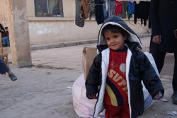 シリアの国内避難民キャンプで、支援物資の防寒着を切る2歳のリマスちゃん。(2018年1月撮影) 