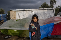 ギリシャのレスボス島モリアにある難民・移民受入・身元確認センターで、滞在するテントの前に立つ女の子。(2018年12月撮影)