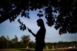 On 30 March 2016, Jessica Marques, 20, checks her mobile phone underneath a tree in a park in Taiobeiras municipality in the Southeastern state of Minas Gerais, Brazil. Jessica was the victim of cyberbullying, social isolation and embarrassment during high school at age 17, when inappropriate images from her mobile phone were shared with her peers in school, following the theft of her phone during summer vacation. The device contained nude images she had taken of herself, but had never shared online. Although Jessica reported the theft to the police, they told her nothing could be done without evidence. The experience left her feeling traumatized and isolated, but her family and a few friends, including Winny Moreira, provided an empowering network of support as she returned to school. Now 20, Jessica works as a hairdresser in Taiboeiras. “I had these pictures of me saved on my phone,” she said. “It got stolen at the sports club by someone who sent out the pictures three days later. I found out when I woke up that morning because of tons of messages people had sent me on Facebook and Whatsapp. I immediately deleted both accounts and I had to turn my phone of because lots of people were calling. People wanted to know what had happened. No one called to give me support, just wanting information and criticizing me.” Jessica continued: “That day, when I found out, I went over to a friend’s house to ask her and her mom for help. Her mom was really supportive and told me she was going to help me. She was the person who told my parents what had happened. This was at the end of summer vacation from school…I didn’t have the courage to go out of the house. My mom didn’t want to believe it and the next day she started to feel really bad. She couldn’t go to work. Everyone was calling her to ask about it all. My dad wouldn’t speak to me about it. I don’t know why. After a few days, he started to speak to me again.” “After the dust settled a bit, my