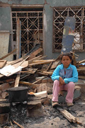 地震により崩壊した家の前にたたずむ少女