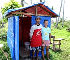 新しく建てられたトイレの前で笑顔を見せる住民