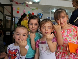 ポリオの予防接種を受けた子どもの指につけられる紫色の印を見せる子どもたち。（イラク）