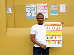 エボラの症状が描かれたポスターを見せる、ケネマ地区の病院で働く薬剤師。（シエラレオネ）