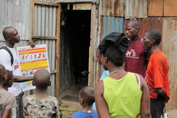 エボラの症状について住民にポスターを見せながら説明をする保健員。（シエラレオネ）