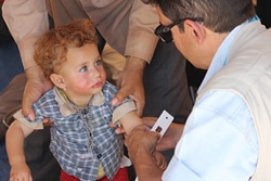 ナウルズ難民キャンプで、栄養状況の検査の一環でヤズディ教徒の子どもの上腕を測るユニセフの保健スタッフ。イラクから逃れてきた多くのヤズディ教徒の人たちは、自宅を離れ避難していたため、食糧や水を持っていない。