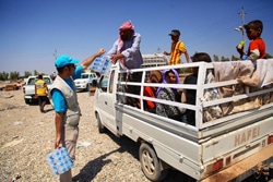 シリアの国境付近で、トラックで避難するヤズディ教徒の子どもや家族に水を配布するユニセフ・スタッフ。
