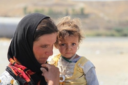幼い子どもを抱いて避難するヤズディ教徒の女性。（イラク）