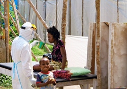 防護服を着てエボラ治療センターで患者に水を飲ませる保健員。（シエラレオネ）