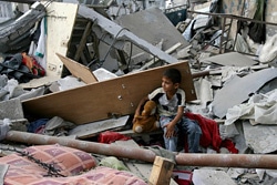 瓦礫の中で、おもちゃを片手に座る男の子。（ガザ）