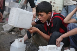 列に並びながら、水を飲む男の子。（シリア）