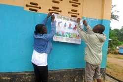 カイラフンで、エボラの症状や予防法が描かれたポスターを壁に貼るスタッフ。（シエラレオネ）