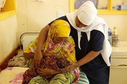 看護師に教えてもらいながら、赤ちゃんに母乳を与える母親。（ケニア）