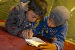 シリアから避難し、レバノンの非公式テント居住区に身を寄せている子どもたち。家族が暮らすテントの家の中でアルファベットの練習をしている様子。