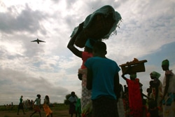 上ナイル州のKiech Kuonで、赤ちゃんを寝かせたバスケットを頭に乗せ、 即応チームによる食糧の空中投下を見守る女性。（南スーダン）