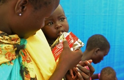 栄養不良の子どもに、すぐ口にできる栄養治療食を与える母親。（南スーダン）
