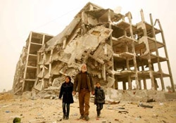 かつて生活を送っていた自宅のある、戦闘で破壊された建物の前を歩くアリさん（中央）と孫のサマールちゃん（左）、ロソルちゃん（右）。