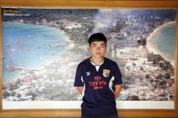 津波に見舞われた町の写真の前で立つノン・ビーさん(タイ)