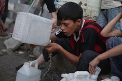 水を汲むための長い列に並びながら、水を分けてもらう少年。（シリア）