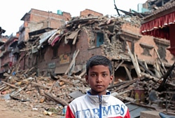 地震で被害を受けた自宅の前でたたずむ11歳の少年。
