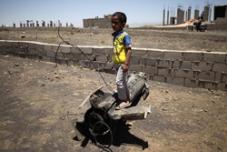 首都サヌア近郊の村で、自宅近くで爆発した砲弾の残骸の上に立つ男の子。