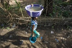 たらいに水を汲んで家に運ぶ女性。