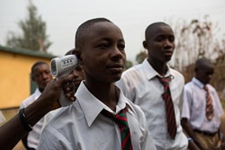 エボラの感染拡大のリスクを最小限にするため、国中の学校の校門で体温検査が行われている。非接触型体温計で体温を測る少年。（シエラレオネ）