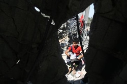 空爆で瓦礫となった自宅から見つかった教科書を見つめる男の子。（パレスチナ・ガザ地区）