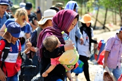 ペットボトルの水を手に、赤ちゃんを抱いて歩く女性。