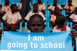 「バック・トゥ・ラーニング」が開始された日、「僕は学校に行くよ！」と書かれた幕を持つ、南スーダンの男の子。