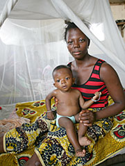 写真：寝台用の蚊帳の下に座る、最近マラリアから回復した女性と子ども